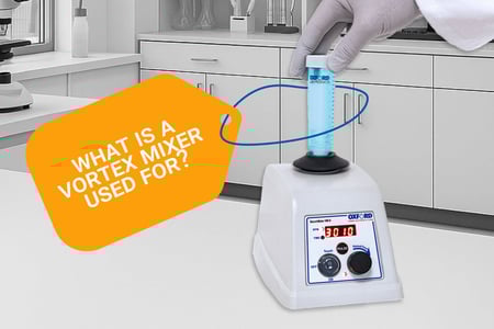 In a lab setting, a white bench-top vortex mixer with a digital display and dial sits on a counter while a gloved hand presses a blue liquid–filled conical tube onto the black rubber cup; a curved arrow indicates the orbital mixing motion. An orange callout asks, “What is a vortex mixer used for?”